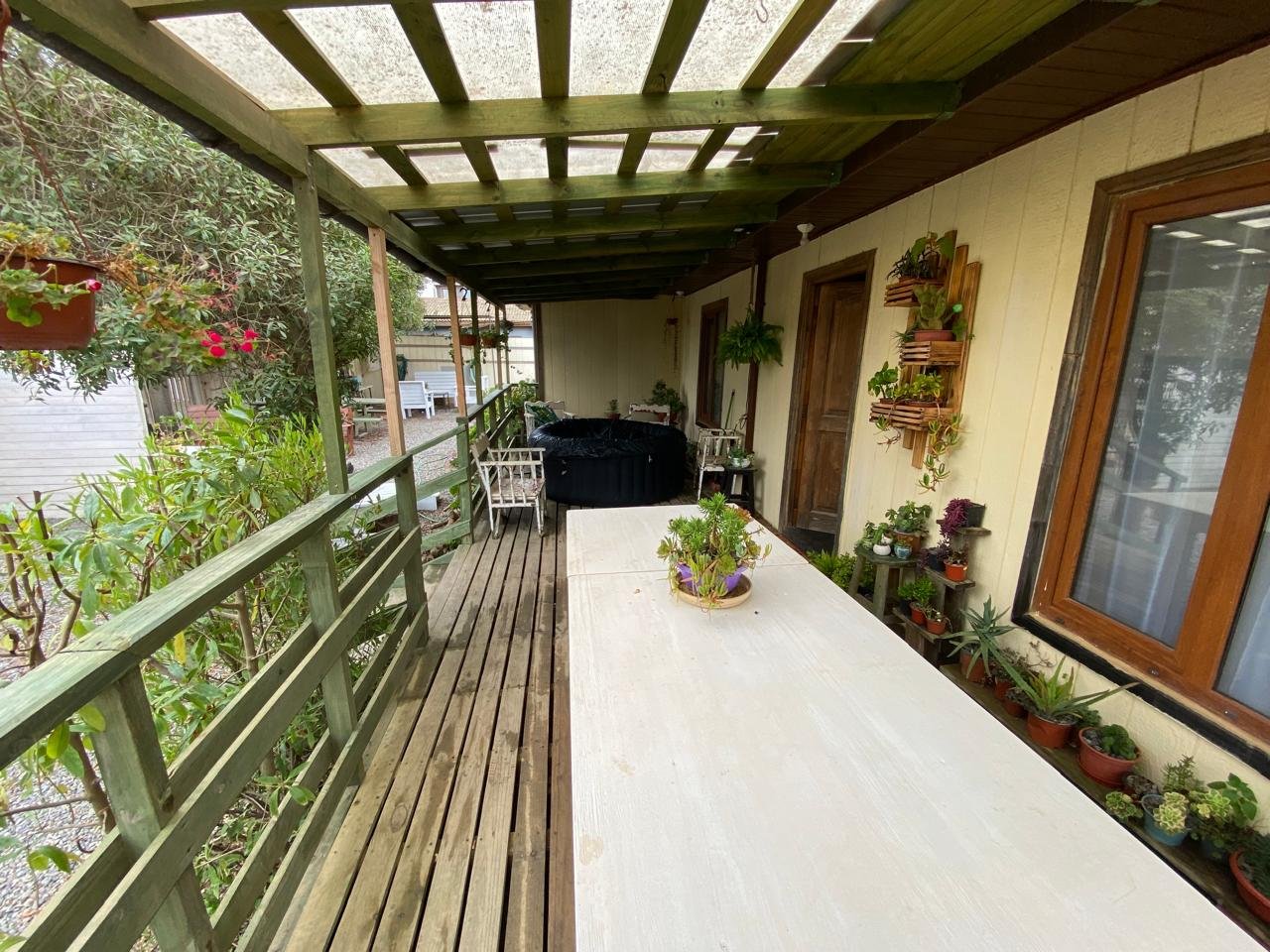 Terraza techada con mesa larga, plantas y sector de descanso